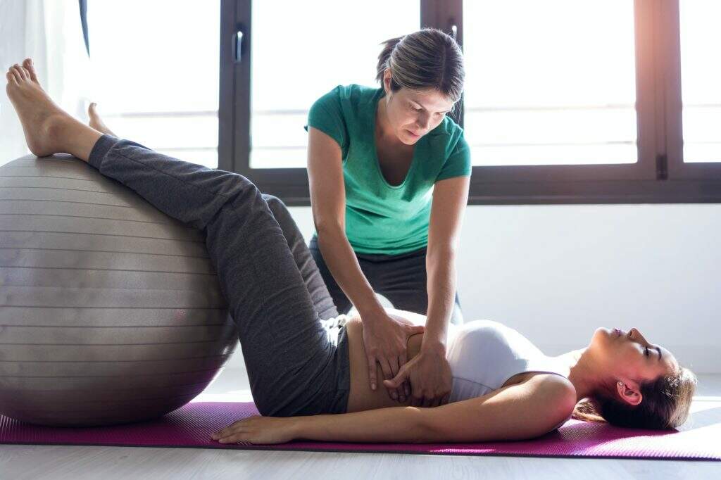 physiotherapist helping to beautiful pregnant woman for doing pilates exercises